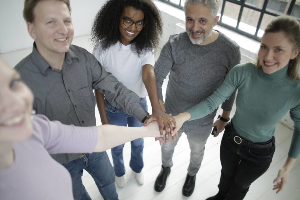 happy diverse coworkers of different ages joining hands together in workspace